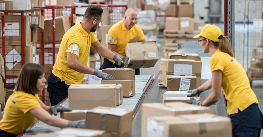 Postal workers sorting packages on a conveyor belt.