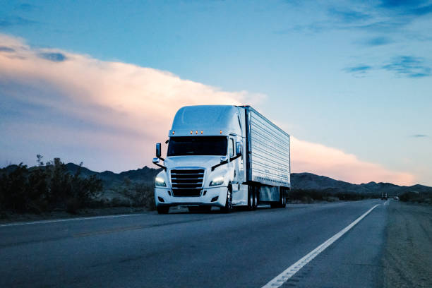 White semi-truck with a large trailer driving on an open highway at sunset