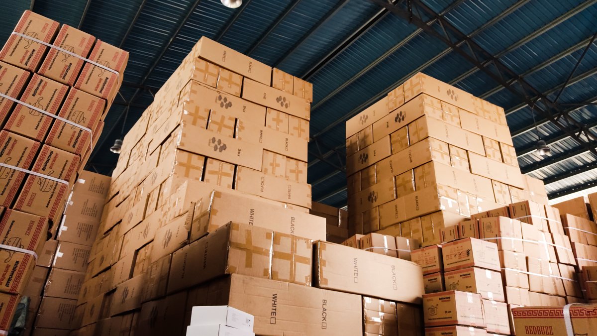 High stacks of cardboard boxes organized in a large warehouse with a blue metal ceiling.